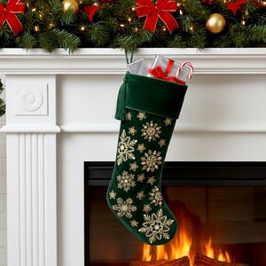 Può includere: Una calza natalizia in velluto verde scuro con motivi a fiocchi di neve ricamati in oro e una nappa verde abbinata. La calza è riempita con scatole regalo argentate con nastro rosso e un bastoncino di zucchero a strisce rosse e bianche.