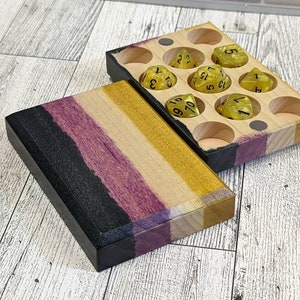 May include: A wooden box with a purple, black, and yellow striped lid. The box is open and contains nine yellow dice with black numbers. The dice are numbered 1 through 6.