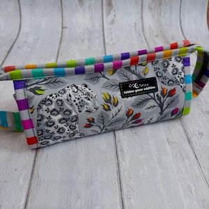 May include: A gray fanny pack with a black and white leopard print design. The bag features a rainbow striped zipper and trim. The text "hidden gems oddities" is visible on a small black tag.