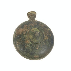 May include: A round, green, metal flask with a small, round opening at the top. The flask has a worn, aged appearance.