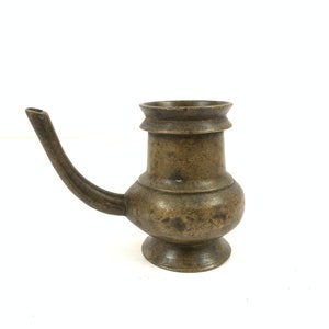 Puede incluir: Una pequeña jarra de agua antigua de latón con un pico y un cuerpo redondeado. La jarra tiene una pátina marrón oscura y está en buen estado.