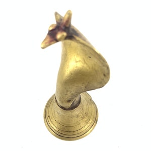 Könnte beinhalten: Eine goldfarbene Metallfigur eines stilisierten Vogels mit langem Hals und einem kleinen Sockel. Der Kopf des Vogels ist zur Seite geneigt und sein Schnabel ist geöffnet.