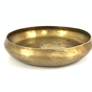 May include: A round, gold-colored metal bowl with a slightly hammered finish. The bowl is empty and has a smooth, reflective surface.