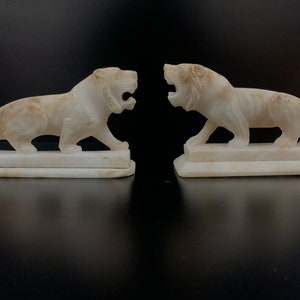 May include: A pair of white marble lion sculptures, each with a roaring expression, standing on a rectangular base.