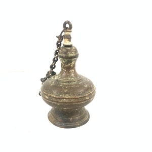 Puede incluir: Una lámpara de aceite antigua de latón con una cadena y una base redonda. La lámpara tiene una pátina desgastada y envejecida.