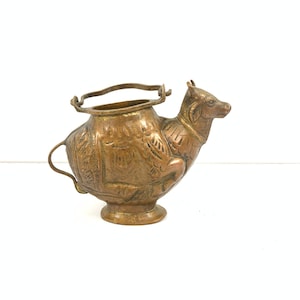 May include: A small, antique brass pitcher shaped like a camel with intricate details and a handle.