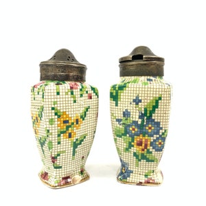 Puede incluir: Un par de saleros y pimenteros vintage con un diseño floral de mosaico. Los saleros son blancos con flores verdes, amarillas y azules. Las tapas son plateadas.