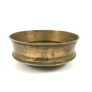 May include: A small, round, brass bowl with a slightly flared rim. The bowl has a worn, aged patina and is perfect for decorative purposes.