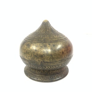 May include: A small, ornate, brass lidded container with intricate engraved designs. The lid is shaped like a dome and the base is round.