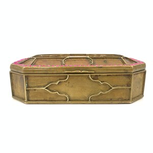 Könnte beinhalten: Eine goldfarbene Metallbox mit einem dekorativen Design und einem rosa Rand um die Oberkante.