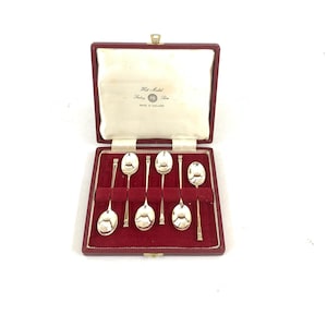 May include: A set of six silver spoons in a red velvet lined box. The box is open, revealing the spoons nestled in individual slots. The box has a cream-colored satin lining on the top and the text "Hall Marked Sterling Silver Made in England".