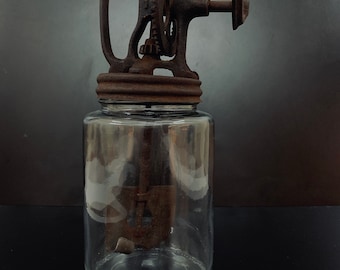 Könnte beinhalten: Antike Butterfässer mit einem Glasgefäß und einer Handkurbel. Das Fässchen ist aus Gusseisen und hat eine rostige Patina. Die Kurbel ist aus Holz und hat einen Metallgriff.