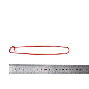 May include: A red knitting needle holder, approximately 21.6 cm long, is shown against a white backdrop. A metal ruler is placed below the needle holder for scale. The needle holder is a simple, elongated loop design.