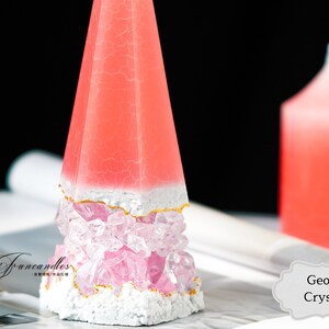 May include: A pink and white geode crystal candle with a gold trim. The candle is shaped like a pyramid and is sitting on a magazine. The text "Geode Crystal" is visible in the image.