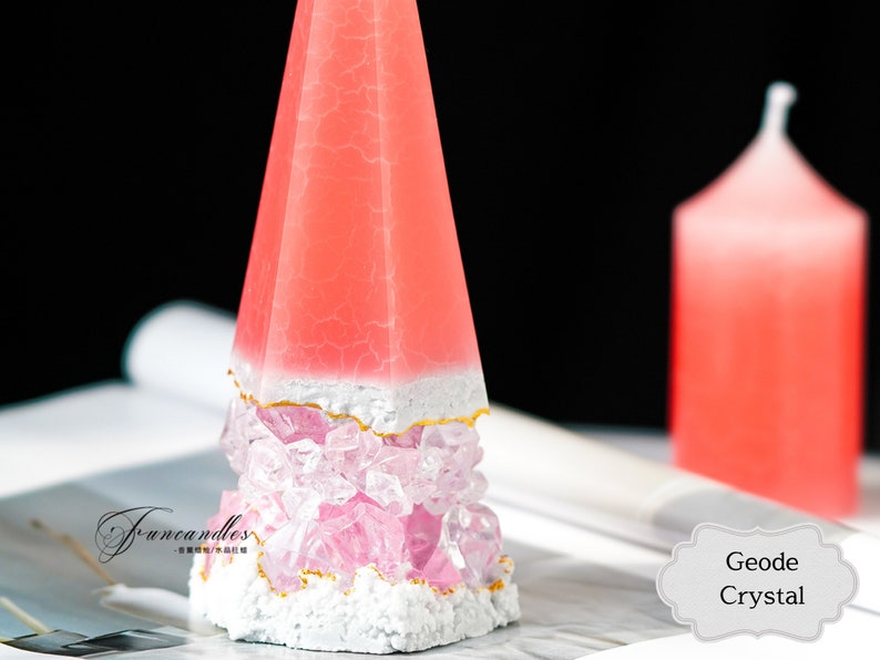 May include: A pink and white geode crystal candle with a gold trim. The candle is shaped like a pyramid and is sitting on a magazine. The text "Geode Crystal" is visible in the image.