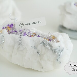 Pu&ograve; includere: Candela bianca a forma di geode con accenti viola e dorati. La candela &egrave; etichettata "FUNCANDLES" e "Ametista Geode".