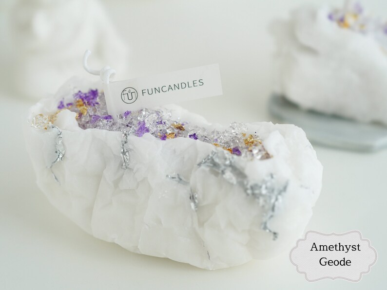 Pu&ograve; includere: Candela bianca a forma di geode con accenti viola e dorati. La candela &egrave; etichettata "FUNCANDLES" e "Ametista Geode".