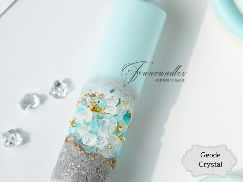 May include: A blue and gray candle with embedded crystals and gold flakes. The candle is labeled "Funcandles - 香薰蠟燭/水蠟燭". The text "Geode Crystal" is also visible in the image.