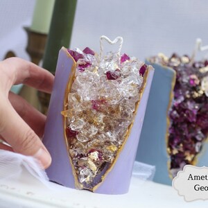 Peut inclure: Deux bougies en forme de g&eacute;ode d'am&eacute;thyste violette avec des accents dor&eacute;s et des cristaux transparents &agrave; l'int&eacute;rieur. Les bougies ont une m&egrave;che en forme de c&oelig;ur blanc.