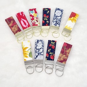 May include: Ten colourful fabric keychains with gold key rings. Each keychain features a different pattern, including floral, geometric, and fruit designs.