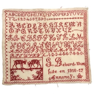 Peut inclure: Un sampler rouge et blanc avec l'alphabet, les chiffres et une petite image brodée de deux cerfs. Le sampler est daté de 1916-17 et signé "G. Debard. Annonay."