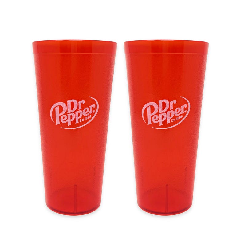May include: Two identical translucent red plastic tumblers, each featuring the white Dr Pepper logo with the text Est. 1885 printed on the front. These cylindrical drinking cups have a smooth finish and a tapered design, standing side by side.