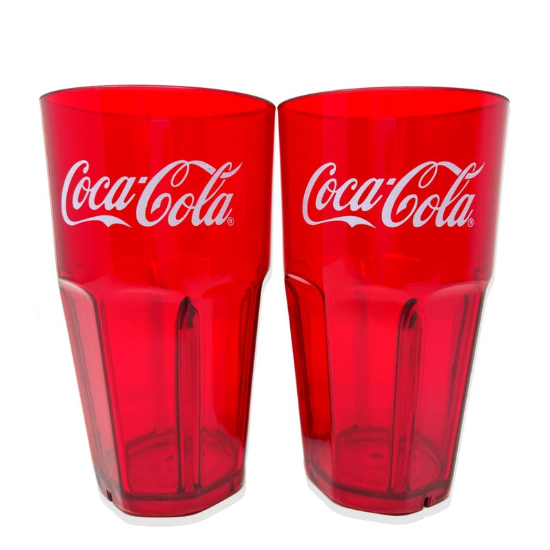 May include: Two translucent red plastic tumblers featuring the white Coca-Cola logo printed on the front. Each cup has a tapered shape with vertical ribbed detailing along the lower sides and a flat base, designed for holding cold beverages.