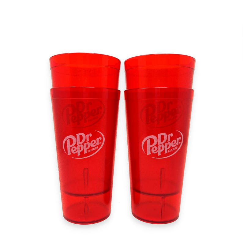 May include: Two translucent red plastic tumblers featuring the white Dr Pepper logo and the text Est. 1885 printed on the front. Each cup has a tapered cylindrical shape with a smooth finish and a slightly thicker base for stability and durability.
