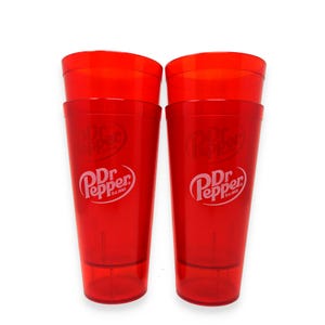 May include: Two tall, translucent red plastic tumblers featuring the white Dr Pepper logo with the text Est. 1885 printed on the front. Each cup has a tapered cylindrical shape with a smooth finish and a slightly thicker base for stability.