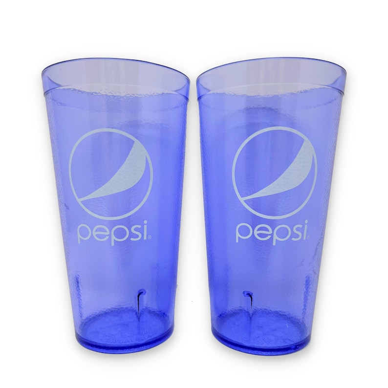 May include: Two translucent blue plastic tumblers featuring the white Pepsi logo and text printed on the front. Each cup has a textured surface and a tapered cylindrical shape with a flat base, designed for serving cold beverages.