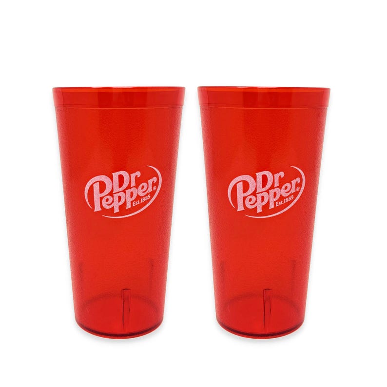 May include: Two identical translucent red plastic tumblers, each featuring the white Dr. Pepper Est. 1885 logo printed on the front. The cups have a tapered cylindrical shape with a smooth finish and a flat base, designed for holding cold beverages.