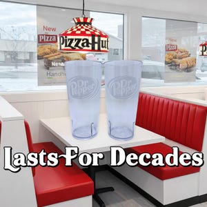 May include: Two clear plastic tumblers featuring the Dr Pepper logo in white, positioned on a white table in a restaurant setting with red booths, a Pizza Hut lamp, and the text Lasts For Decades displayed prominently at the bottom of the image.