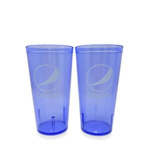 May include: Two translucent blue plastic tumblers featuring the white Pepsi logo and text printed on the front. Each cup has a textured exterior surface, a wide rim, and a tapered base design, providing a consistent look for both beverage containers.