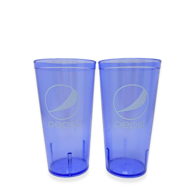 May include: Two translucent blue plastic tumblers featuring the white Pepsi logo and text printed on the front. Each cup has a textured exterior surface, a wide rim, and a tapered base design, providing a consistent look for both beverage containers.