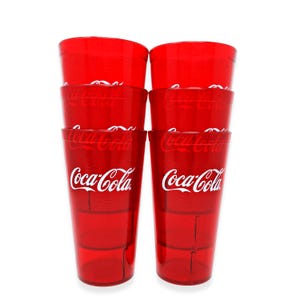 May include: A stack of six red Coca-Cola plastic drinking glasses. The Coca-Cola logo is printed in white on the front of each glass. The glasses are transparent and have a ridged design.