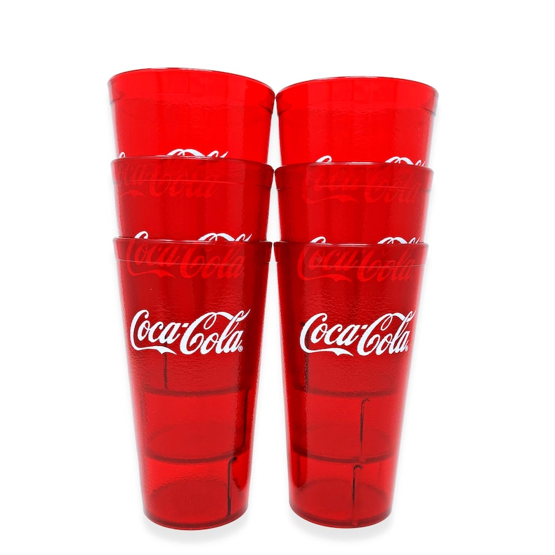 May include: A stack of six red Coca-Cola plastic drinking glasses. The Coca-Cola logo is printed in white on the front of each glass. The glasses are transparent and have a ridged design.
