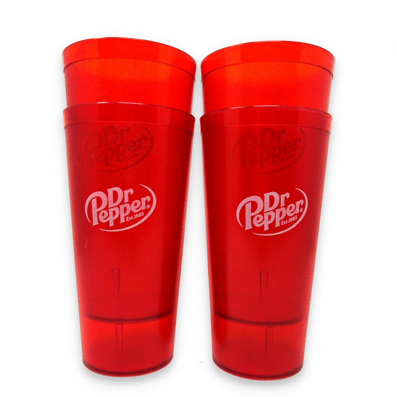 May include: Two tall, translucent red plastic tumblers featuring the white Dr Pepper logo and the text Est. 1885 printed on the front. Each cup has a smooth, cylindrical shape with a slightly wider rim and a flat base, designed for cold beverages.