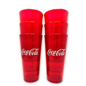 May include: Six red plastic Coca-Cola glasses stacked in two columns of three. Each glass has the Coca-Cola logo in white. The glasses are transparent and appear to be empty.