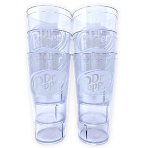 May include: A set of six clear plastic tumblers stacked in two columns of three. Each tumbler features a textured surface and a white etched Dr Pepper logo with the text Est. 1885. The cups have a tapered cylindrical shape with a smooth rim.