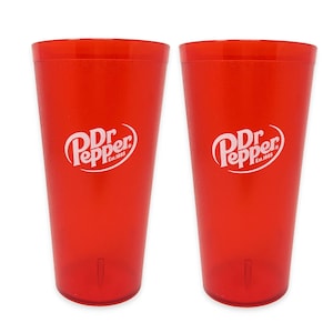May include: Two identical translucent red plastic tumblers, each featuring the white Dr Pepper logo with the text Est. 1885 printed on the front. These tall, cylindrical drinking cups have a smooth finish and a slightly tapered base design.