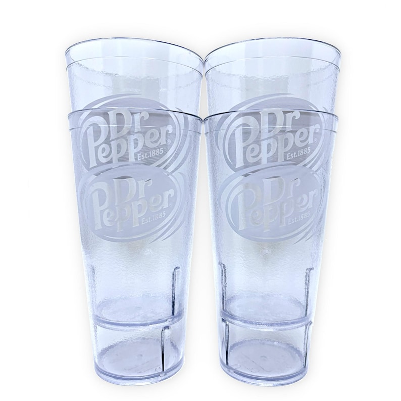 May include: Two clear, textured plastic tumblers featuring the Dr Pepper logo and the text Est. 1885 etched on the front. Each tall, cylindrical cup has a stackable design with a reinforced base and a smooth rim, showcasing a transparent finish.