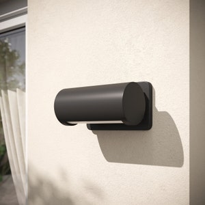 May include: A black cylindrical outdoor wall light fixture with a rounded end. The light is mounted on a white wall.