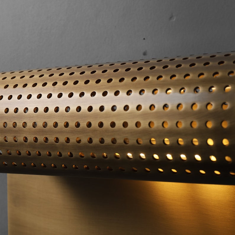 May include: A brass wall sconce with a cylindrical shade featuring a perforated pattern. The light is on and illuminates the room.