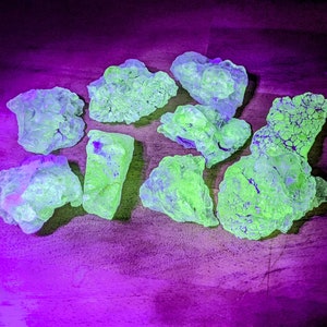 May include: A collection of green and blue fluorescent rocks with a rough, textured surface. The rocks are arranged on a purple surface.