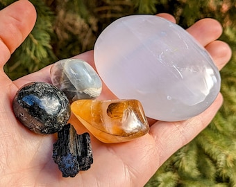 May include: A collection of six polished stones, including a large white selenite, a black obsidian, a grey moonstone, a brown tiger's eye, and a black tourmaline.