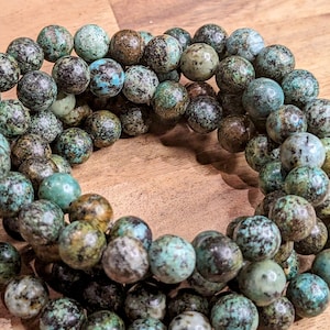 May include: A strand of turquoise beads with a mottled green and brown pattern. The beads are round and have a smooth, polished finish.