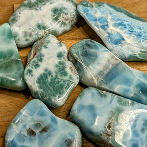 May include: A collection of seven polished blue and green ocean jasper stones. The stones are smooth and have a variety of shapes and sizes.