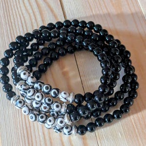 May include: A black beaded bracelet with a white and black patterned bead accent. The bracelet is made of multiple strands of beads.