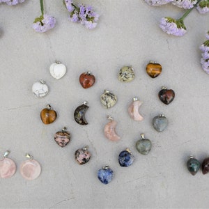 May include: Assortment of heart-shaped and crescent moon-shaped gemstone pendants with silver bail. The pendants are arranged in a heart shape on a light grey background.
