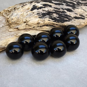 May include: A group of ten black glass marbles on a piece of driftwood.